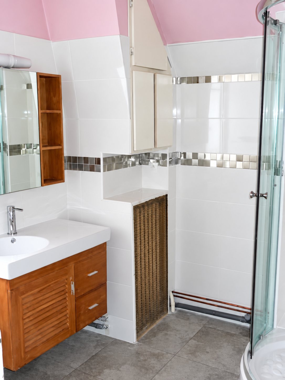 Salle de bains rénovée aux murs carrelés de blanc avec une frise de mosaïque, un meuble vasque en bois et une cabine de douche d’angle en verre.